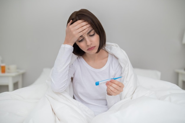 Unwell young woman checking body temperature at home