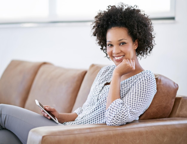 Unwinding at home with my tablet Portrait of an attractive woman sitting on the sofa with her smartphone