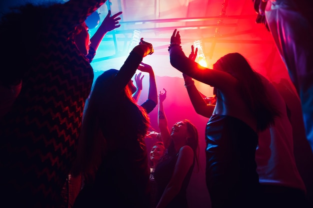 Upcoming. A crowd of people in silhouette raises their hands on dancefloor on neon light background. Night life, club, music, dance, motion, youth. Purple-pink colors and moving girls and boys.