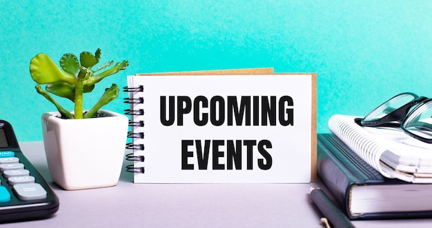 UPCOMING EVENTS is written on a white card next to a potted flower, diaries and calculator