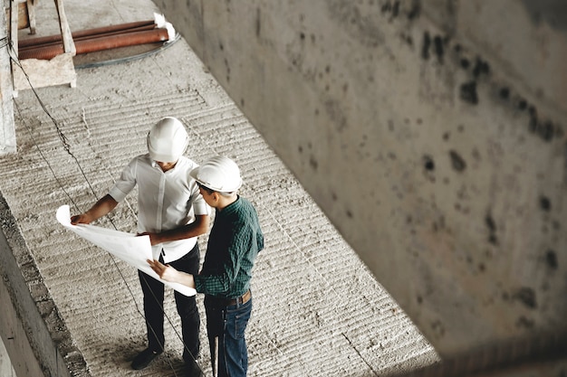 Upper view of a adult arhitecht and his worker talking about building in constructiion being on the worksite.