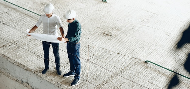 Upper view portrait of two engineers looking at the building's plan while holding a map