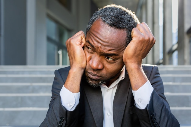 Upset african american man sitting on stairs outside office building businessman bankrupt in despair