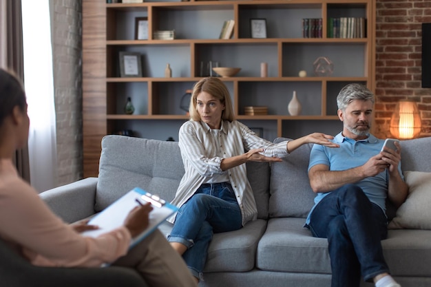 Upset angry european wife swears at husband with smartphone in office clinic interior Problems in marriage