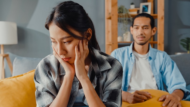 Upset asian couple sit on couch in living room