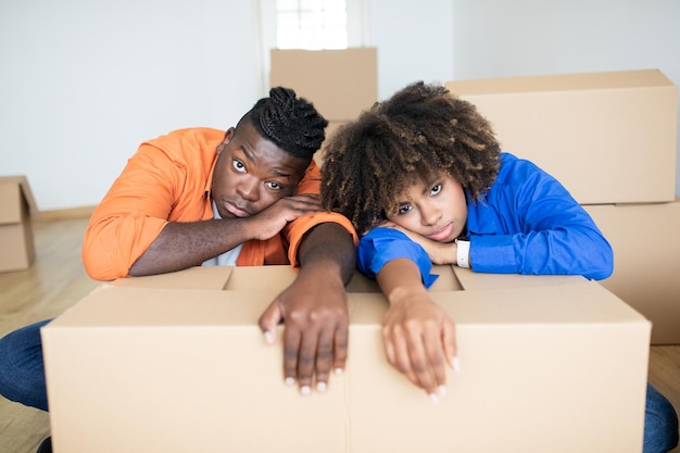 Upset black spouses leaning at cardboard box having stress while moving home