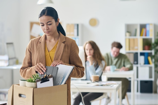 Upset businesswoman packing her things in box during leaving from her workplace