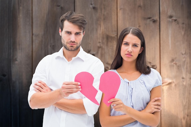 Upset couple holding two halves of broken heart against wooden background