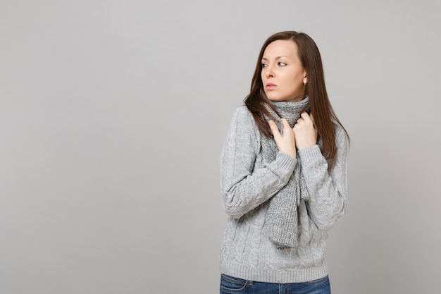 Upset displeased young woman in gray sweater, scarf looking aside isolated on grey wall background in studio. Healthy fashion lifestyle people sincere emotions cold season concept. Mock up copy space.