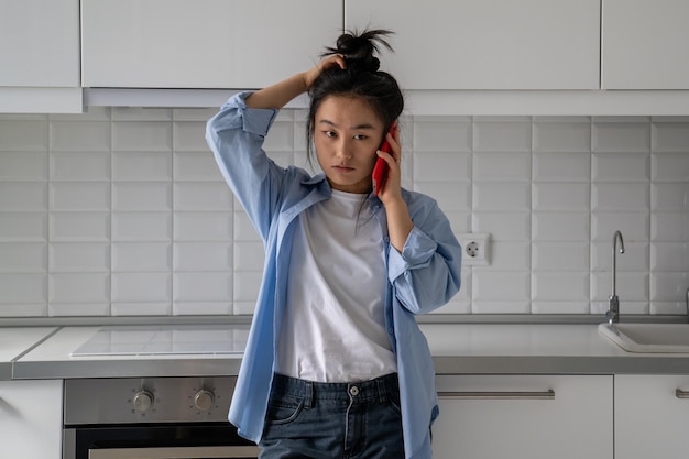 Upset dissatisfied young asian woman talking on phone arguing by mobile at home