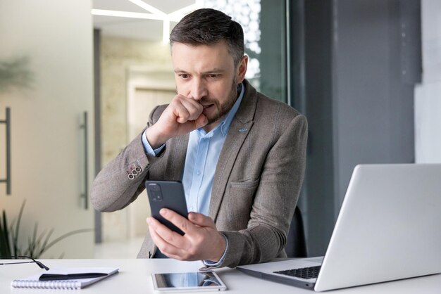 Upset frustrated man holding phone inside office sad businessman reading bad news online boss