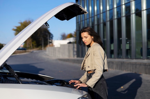 Upset girl opened the hood of a car on the street near a modern glass building Car broke down maintenance service