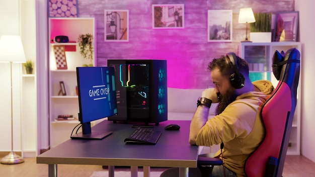 Upset professional game player after losing an important online game. Gamer playing in a room with colorful neon lights.