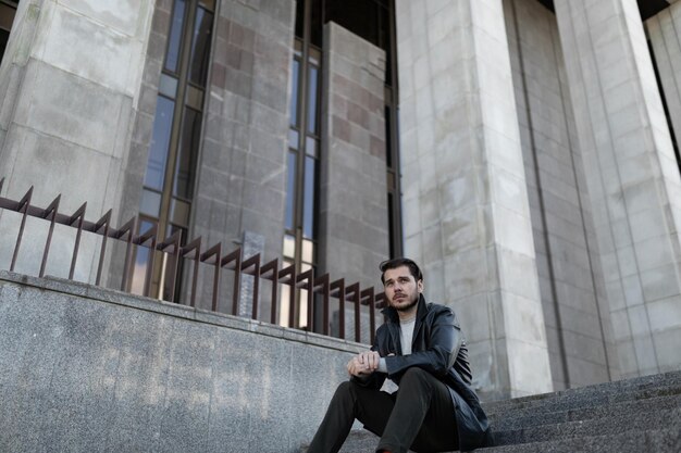 Upset sad man sitting on the steps near the gray building