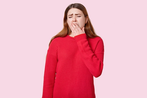 Upset sleepy woman yawns and covers mouth with palm