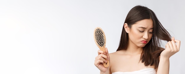 Upset stressed young Asian woman holding damaged dry hair on hands over white isolated background