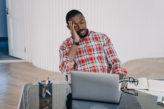 Upset tired african american businessman sitting at laptop suffer from headache Difficulties in job