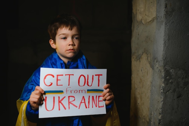 Upset Ukrainian poor toddler boy kid homeless protesting war conflict raises banner with inscription massage text No War on black background Crisis peace stop aggression child against Russian war