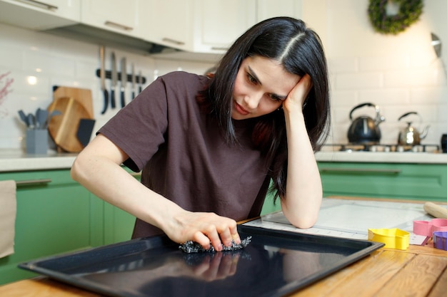 Upset woman cleaning a baking sheet in the kitchen tired of household chores