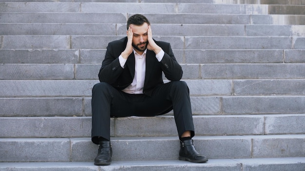 Upset young business man having stress and sitting on stairs in street