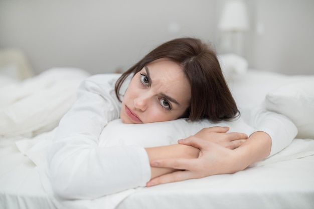 Upset young woman feeling lonely lying on bed at home