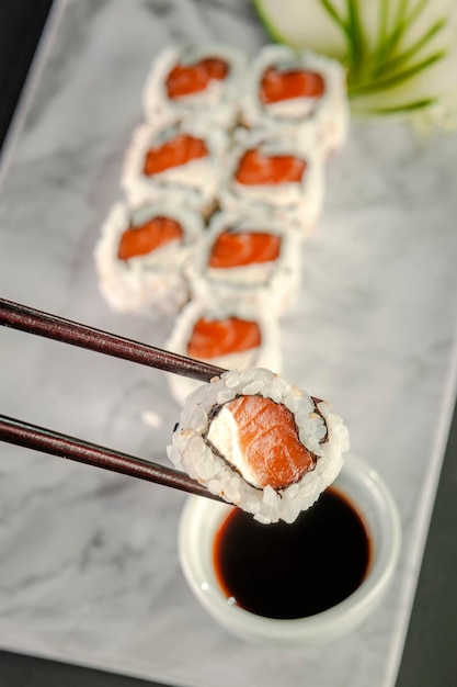 Uramaki salmon on chopsticks with soy sauce. Closeup.