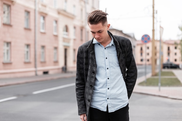 Urban stylish young guy with trendy hairstyle in fashionable elegant clothes  near vintage houses outdoors.