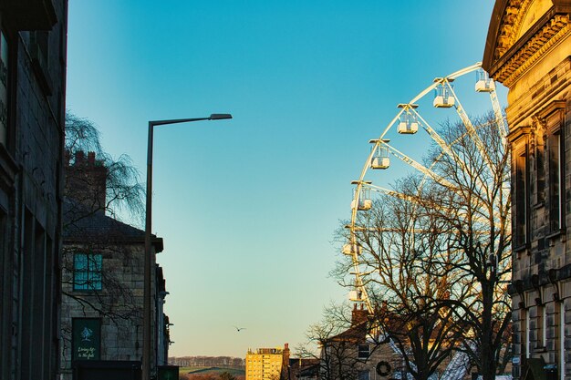 Photo urban sunset scene with silhouette of a ferris wheel against a clear sky flanked by historic buildings and a street lamp in lancaster