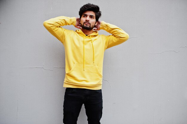 Photo urban young hipster indian man in a fashionable yellow sweatshirt cool south asian guy wear hoodie against grey wall