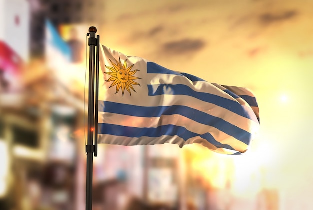 Uruguay Flag Against City Blurred Background At Sunrise Backlight