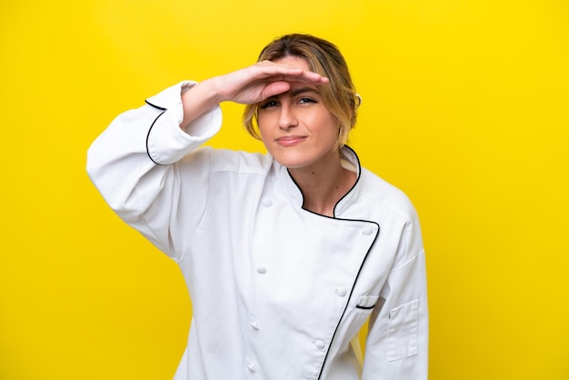 Uruguayan chef woman isolated on yellow background looking far away with hand to look something