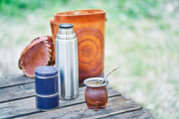 Uruguayan Mate Kit Lined in Leather, with the light bulb, thermos and bag on a wooden table in the countryside