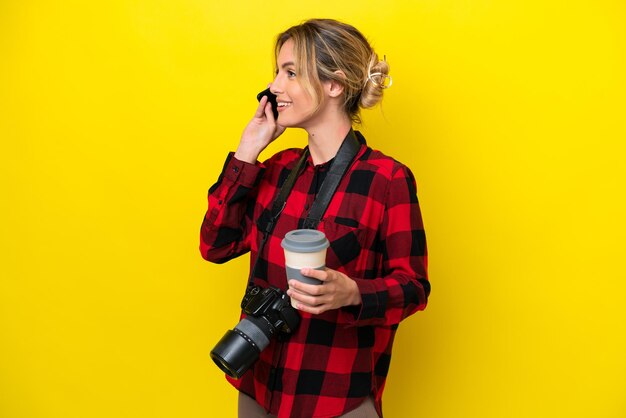 Uruguayan photographer woman isolated on yellow background holding coffee to take away and a mobile