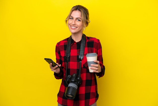 Uruguayan photographer woman isolated on yellow background holding coffee to take away and a mobile