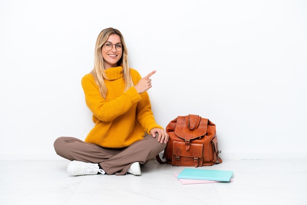 Uruguayan student woman sitting one the floor isolated on white background pointing to the side to present a product