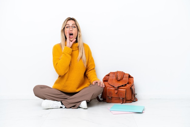 Uruguayan student woman sitting one the floor isolated on white background shouting with mouth wide open