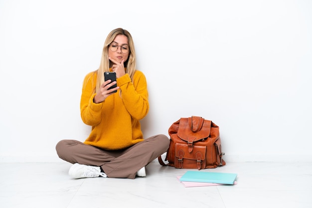 Uruguayan student woman sitting one the floor isolated on white background thinking and sending a message