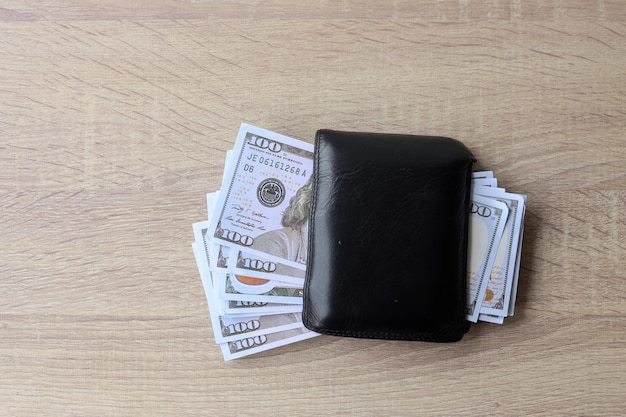 US dollar money in black leather wallet on wooden table. Top view.