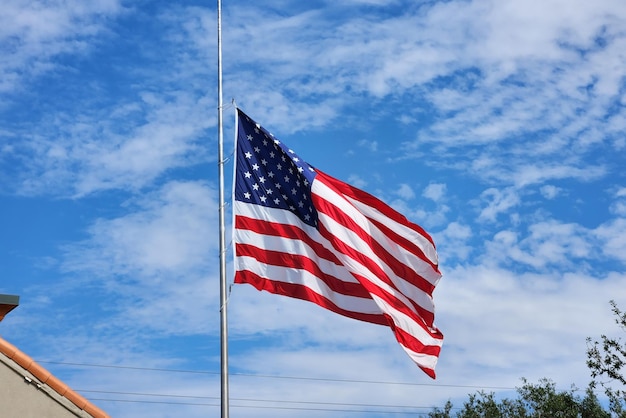 USA national flag waving lowered to half mast on wind against blue sky American stars and stripes spangled banner as symbol of democracy