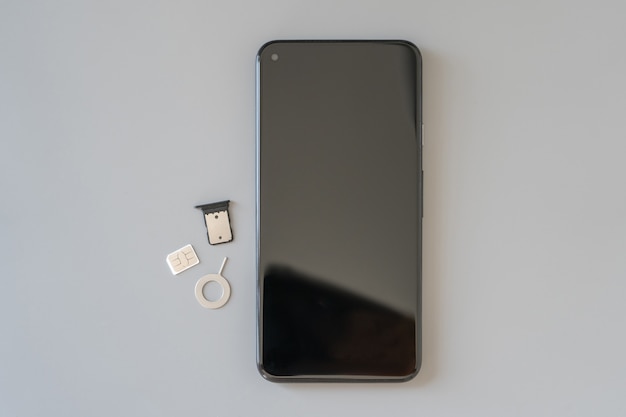 The used Nano-SIM (4FF), the tray removed from the slot and the extractor for extracting the SIM card and the smartphone are on the table