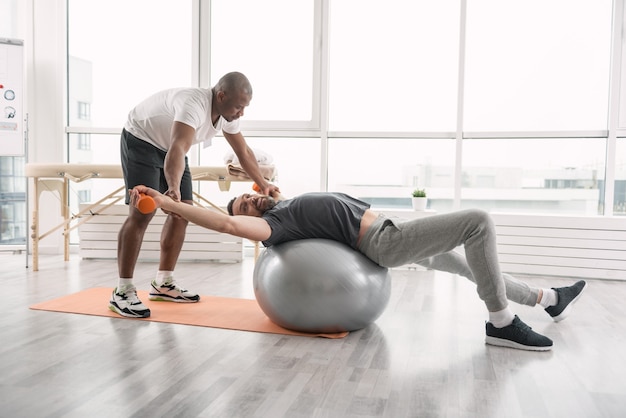 Useful activities. Joyful happy man lying on the med ball while enjoying the training