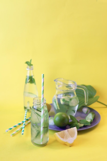 Useful cocktail of lemon slices limes mint leaves in glass bottles on a yellow background