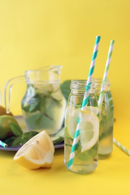 Useful cocktail of lemon slices limes mint leaves in glass bottles on a yellow background