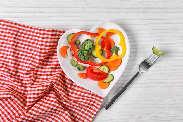 Useful cut vegetables on a plate in the form of heart on wooden table top view