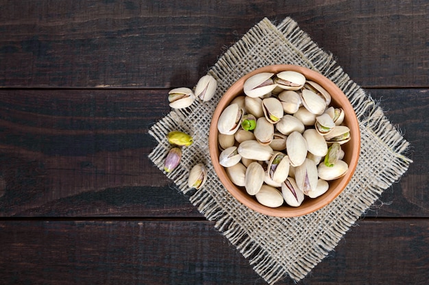 Useful nuts - pistachios in a ceramic bowl on a dark wooden.