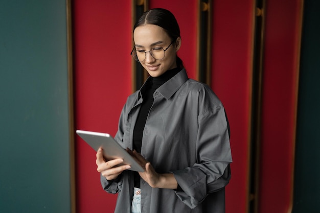 Uses a tablet a confident business woman with glasses looks away is in an office coworking space