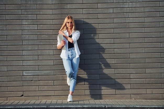 Photo using laptop beautiful blonde in casual clothes is outdoors at sunny daytime