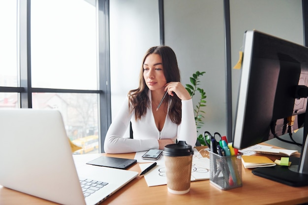 Using laptop Young adult woman in formal clothes is indoors in the office