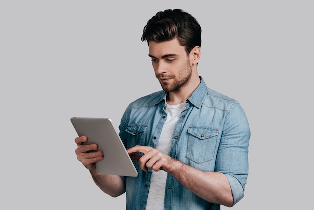 Using modern technologies. Casual guy posing against the white wall