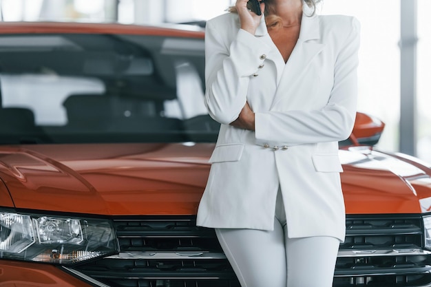 Using phone Woman in formal clothes is indoors in the autosalon